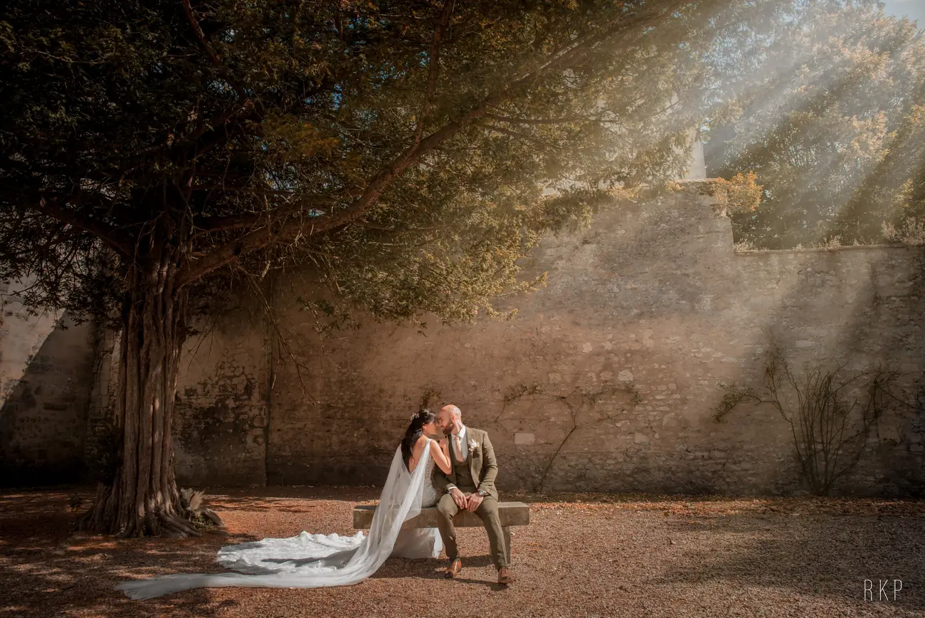 Mariés sur un banc de pierre sous un arbre, rayons de soleil